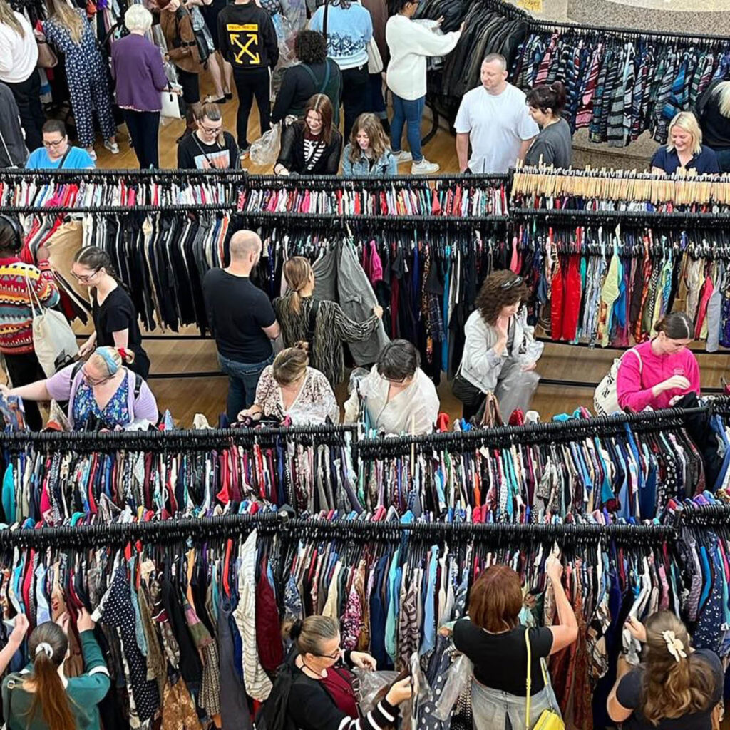Rows upon rows of rails are filled with pre-owned clothes at the Vintage Kilo Sale, Newcastle. Several people browse the rails.