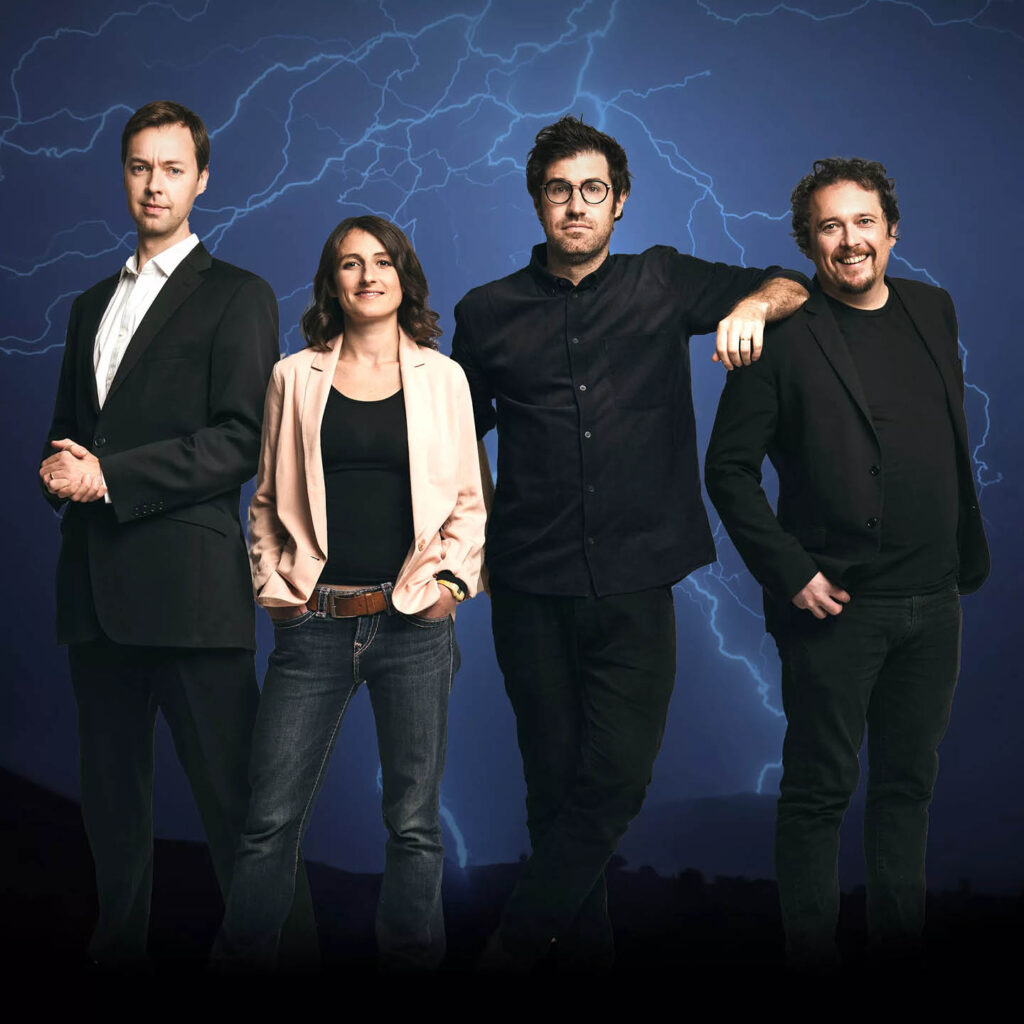 The four presenters of No Such Thing As A Fish stand in a row against a blue backdrop with lightning strikes.