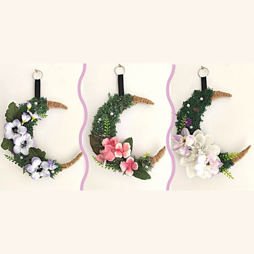 Three hanging decorations decorated with green foliage. Each one has different coloured flowers attached to it - lilac, pink and white.