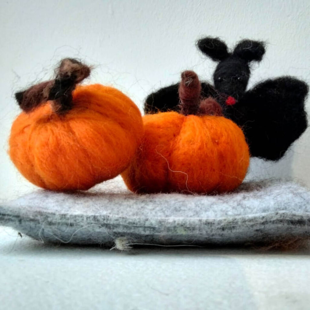Two orange needle felted pumpkins and a black needle felted bat.
