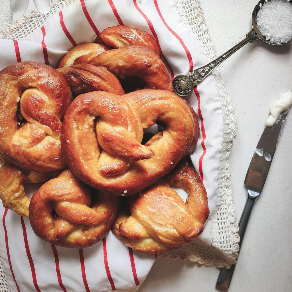 A red and white striped cloth is covered with a pile of golden pretzels.