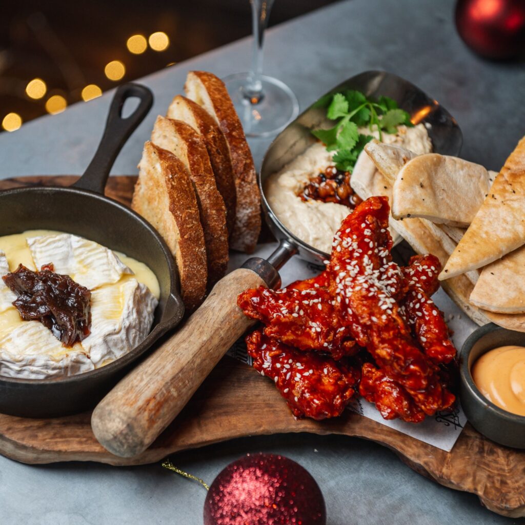 A large spread of mouthwatering appetisers featuring creamy humus, korean fried chicken and baked Camembert