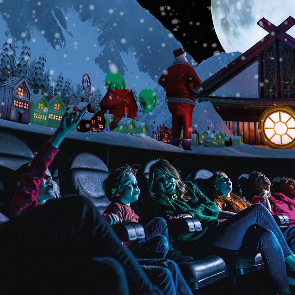 A row of adults and children sit in the Life Science Centre's planetarium. They point and gaze in wonder as the domed ceiling displays a Christmas scene.