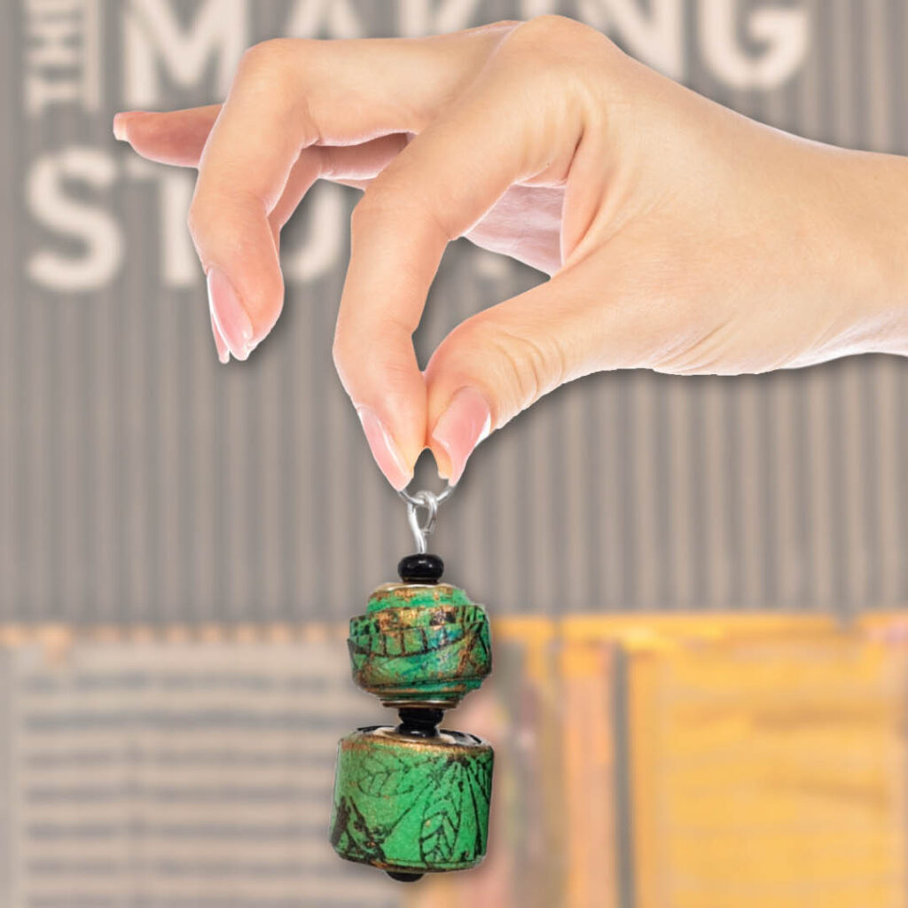 A hand holds up a single earring. It is chunky and green and features a leaf pattern.