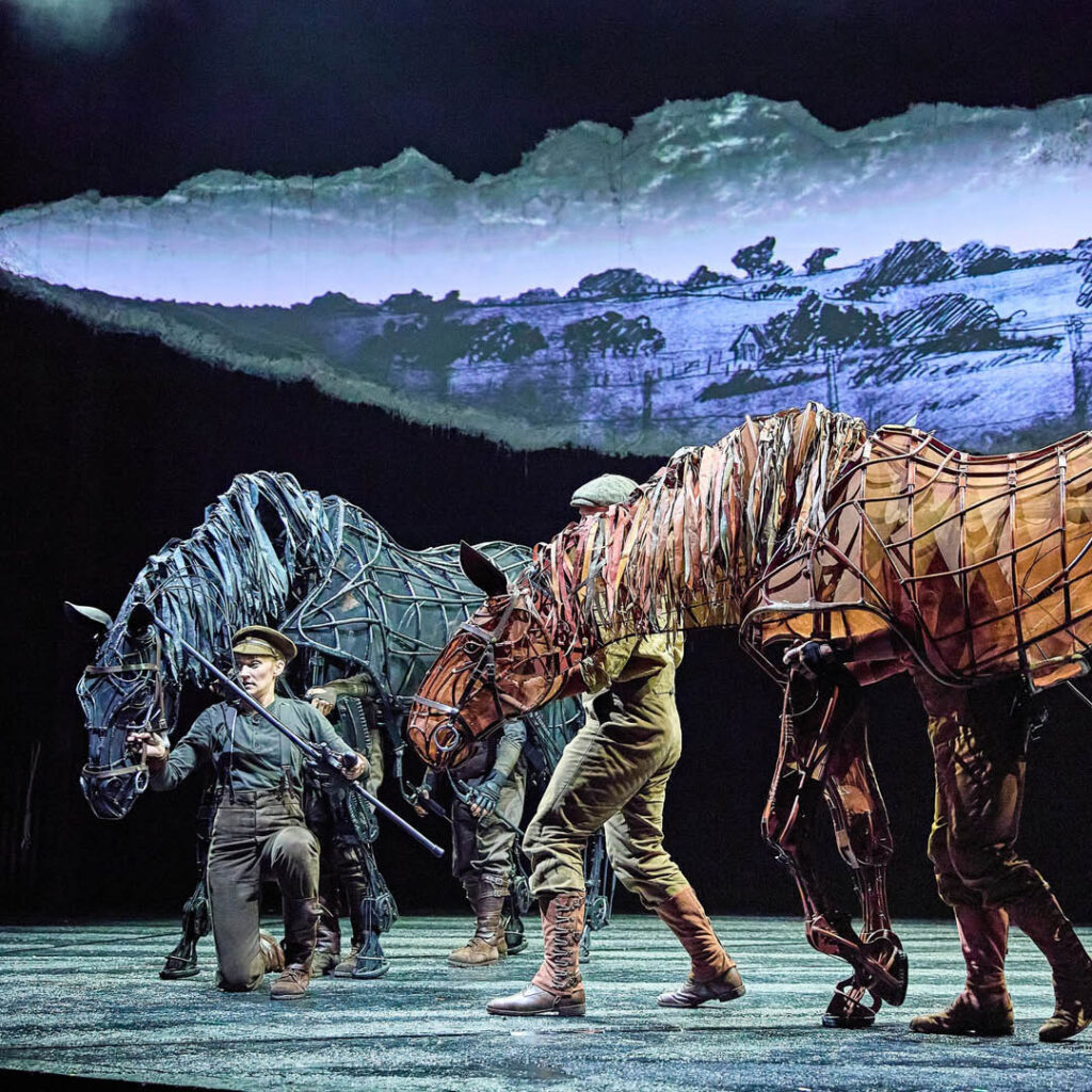 Two men dressed on wartime soldier costumes leads life size horse puppets across the stage at Sunderland Empire.
