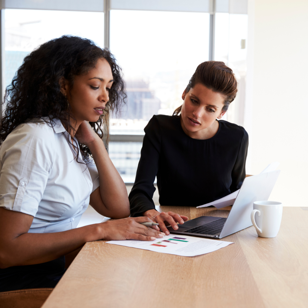 Two women sit in an office looking at a laptop together