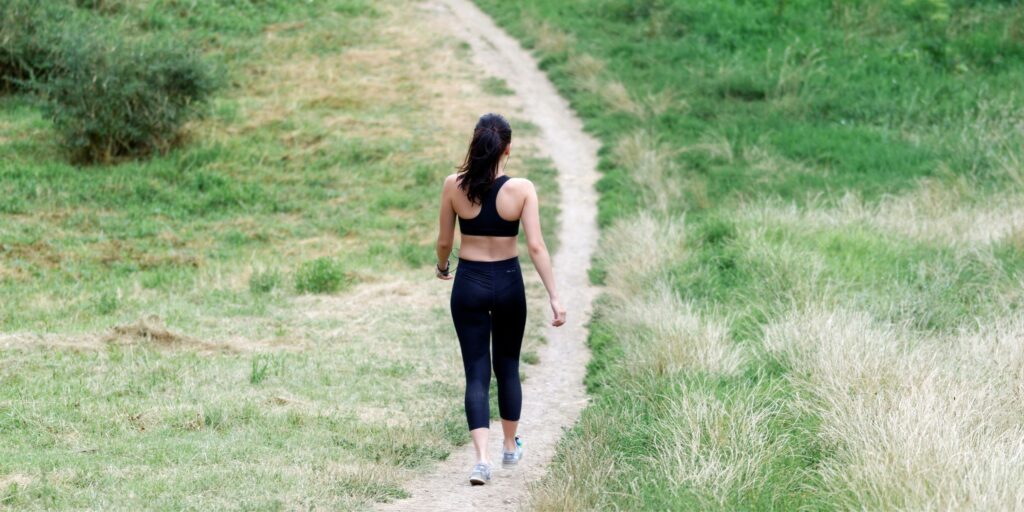 A girl in a black workout set walks along a green path