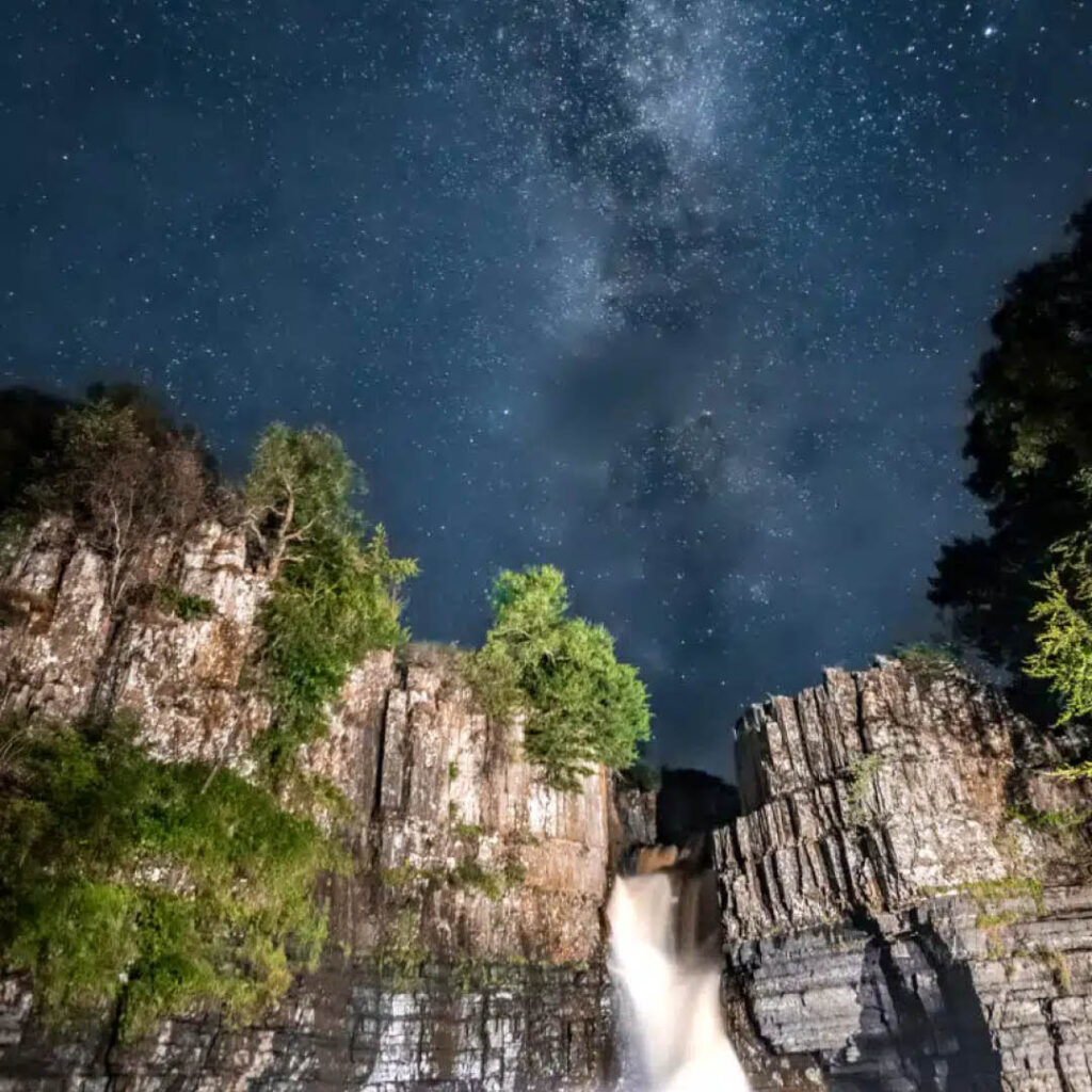 A starry night sky above High Force waterfall.