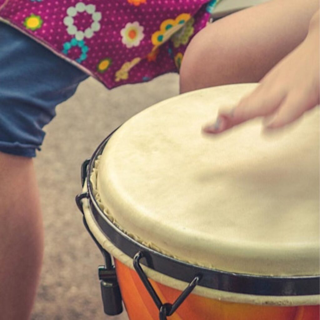 A child beats a hand against an African drum.