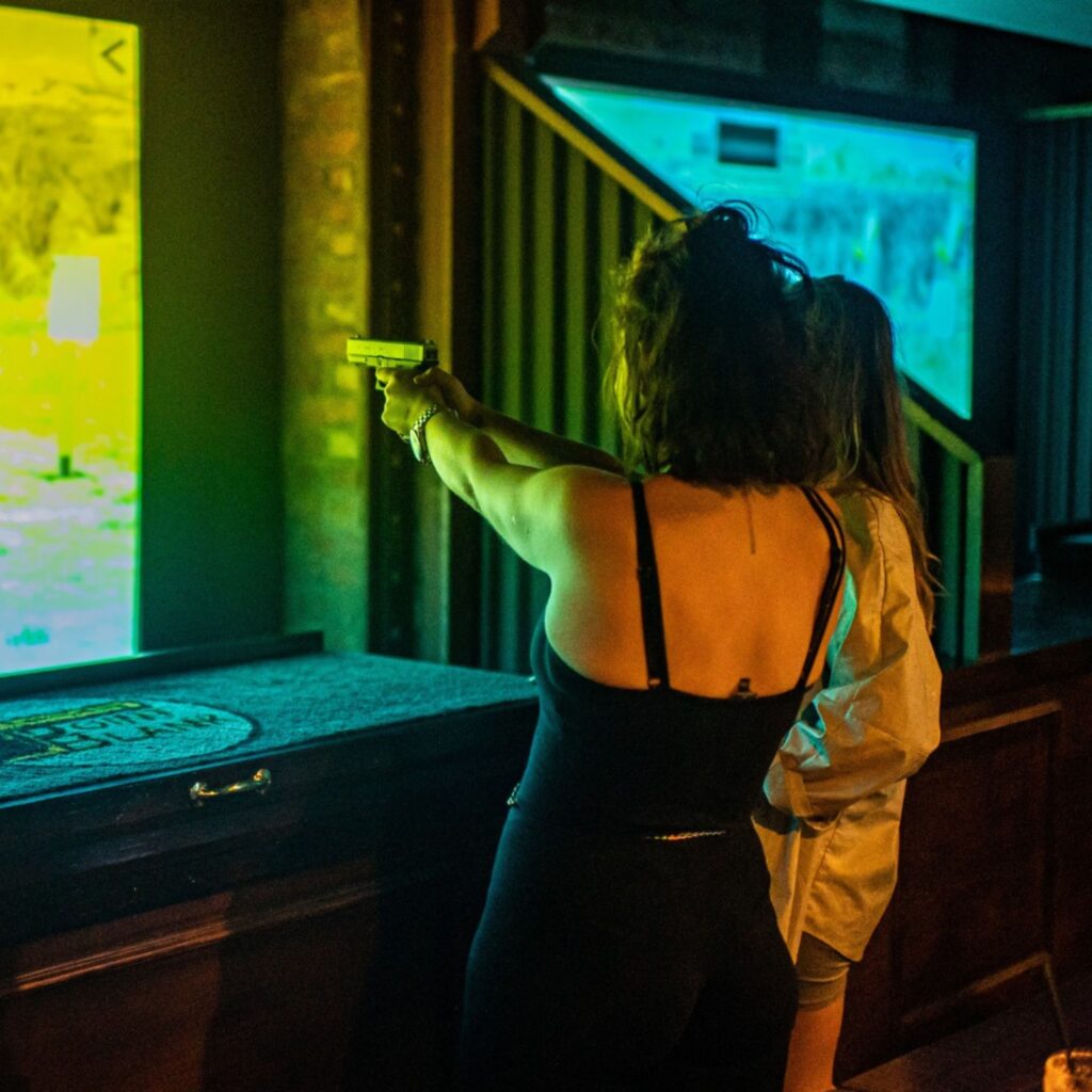 A girl in a black dress raises a gun to a screen. She is at Point Blank Shooting in Newcastle.