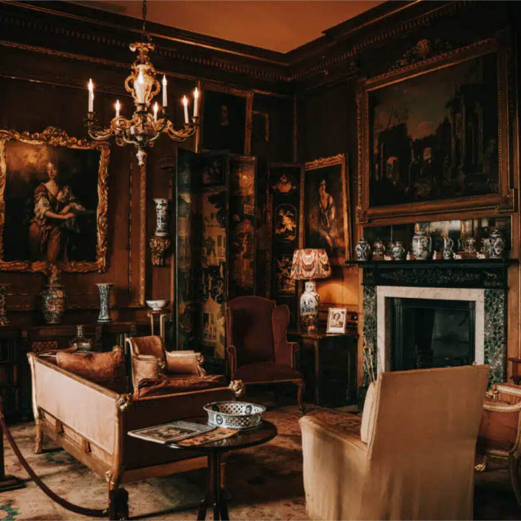A dimly lit living room in Raby Castle features a chandelier, plush sofas and armchairs and paintings on the walls and above the fireplace.