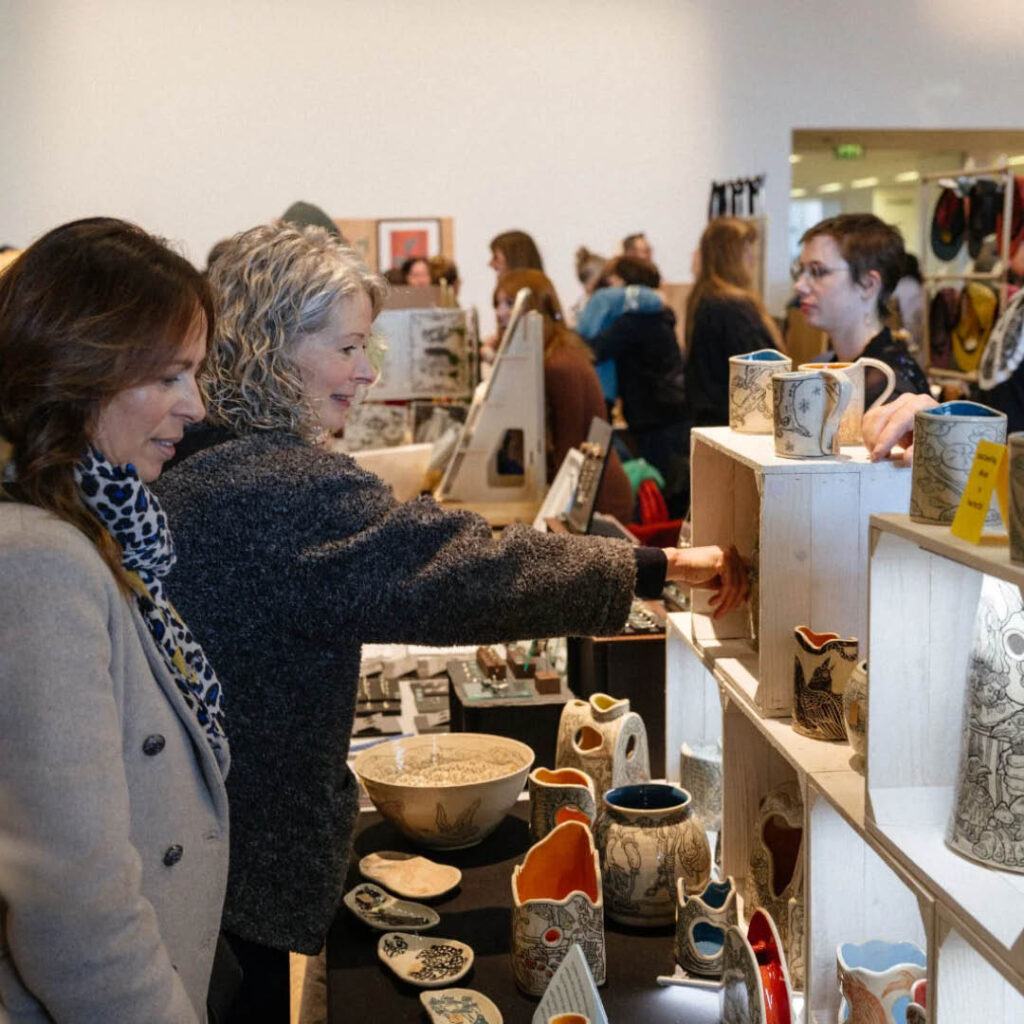 Two women smiles as they browse a handmade ceramics stall at the BALTIC's Spring Makers Market.