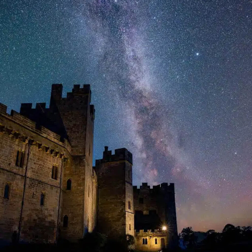 Raby Castle is silhouetted against a purplish blue sky studded with thousands of stars.
