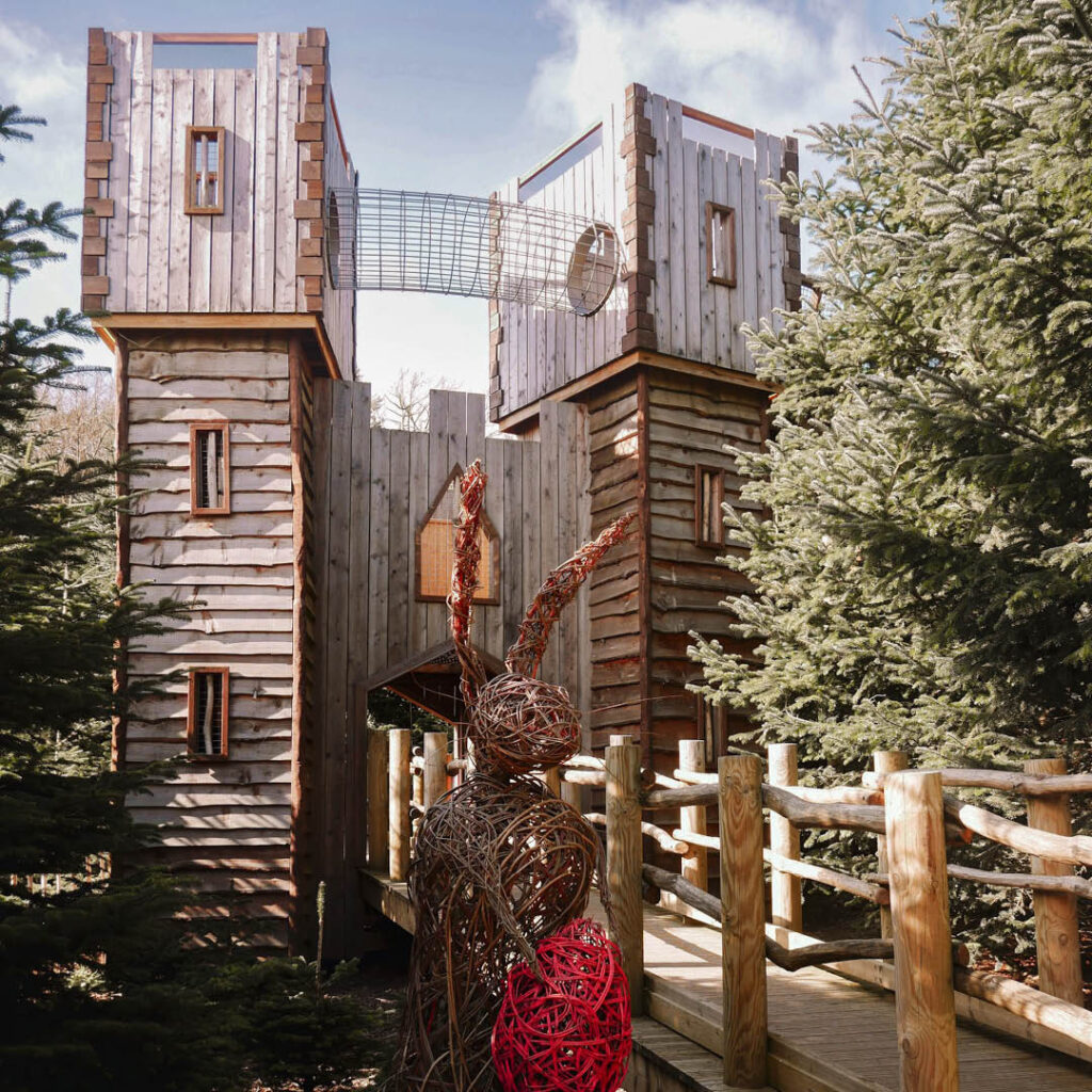 A wooden play structure is surrounded by trees at Raby Castle. A big woven sculpture of a rabbit with a red egg stands in front of it.