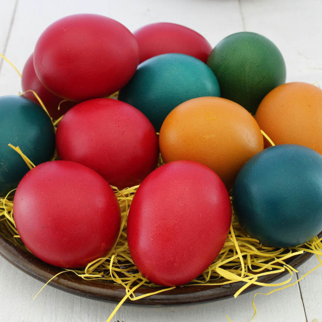 Eggs painted in different colours are piled onto a bed of straw.