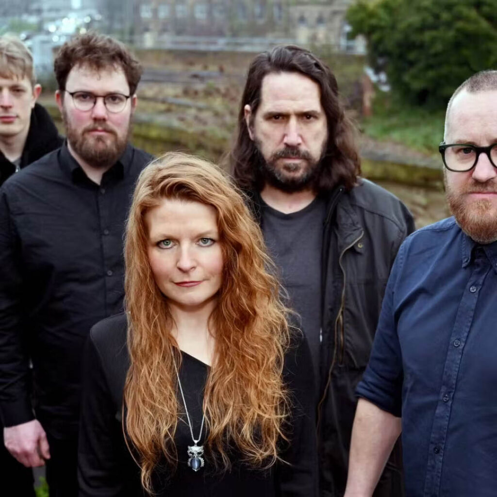 Members of the band Living in Shadows stare seriously at the camera in an outdoor setting.