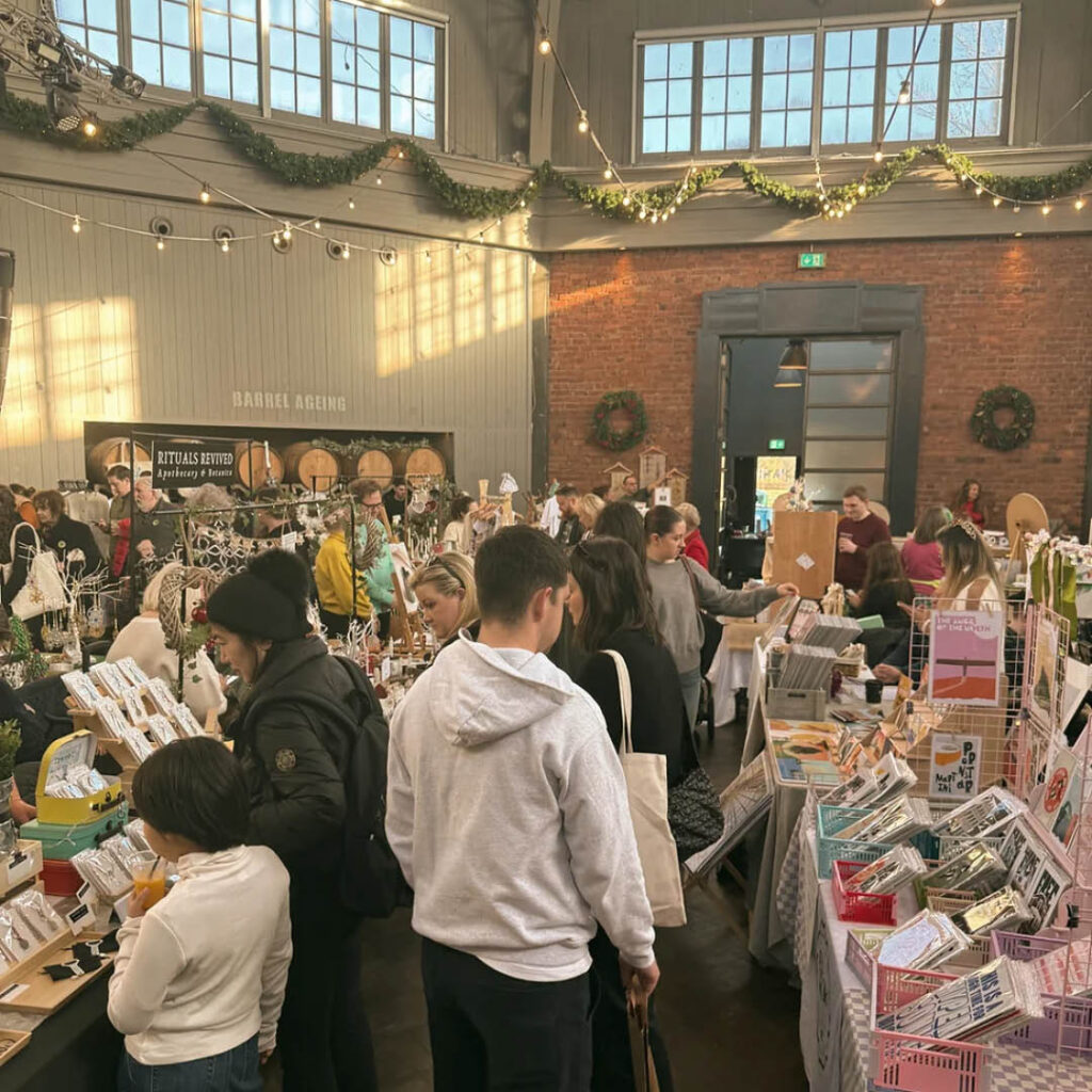Lots of people wander around art and craft stalls at The Crafty Bazaar's Christmas market. Festive garland and wreaths decorate the brick walls of Wylam Brewery's main hall.
