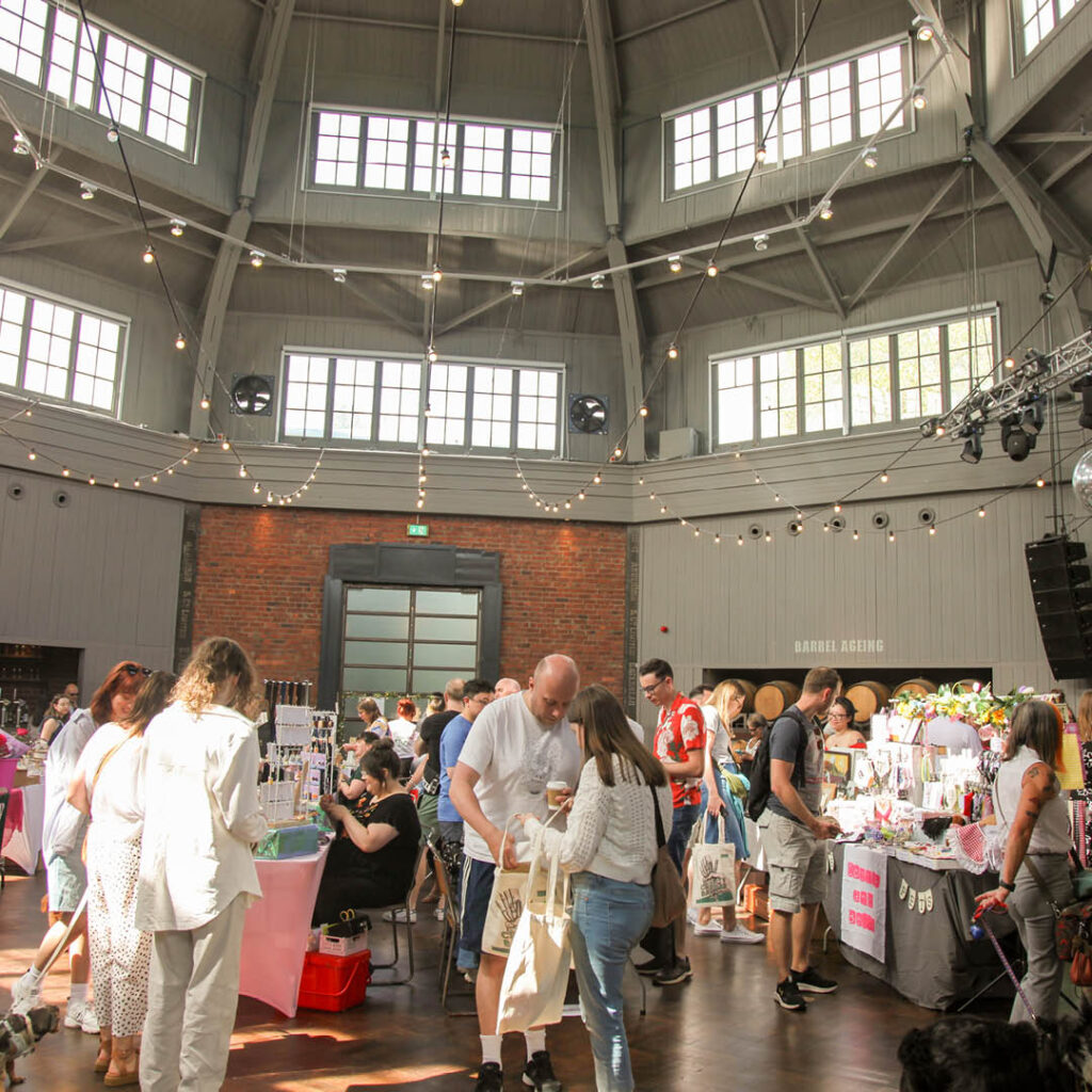 Sunlight streams into Wylam Brewery's main hall through skylights. Lots of people browse stalls selling a range of local crafts and goods. This is the Crafty Bazaar's Summer Makers Market.