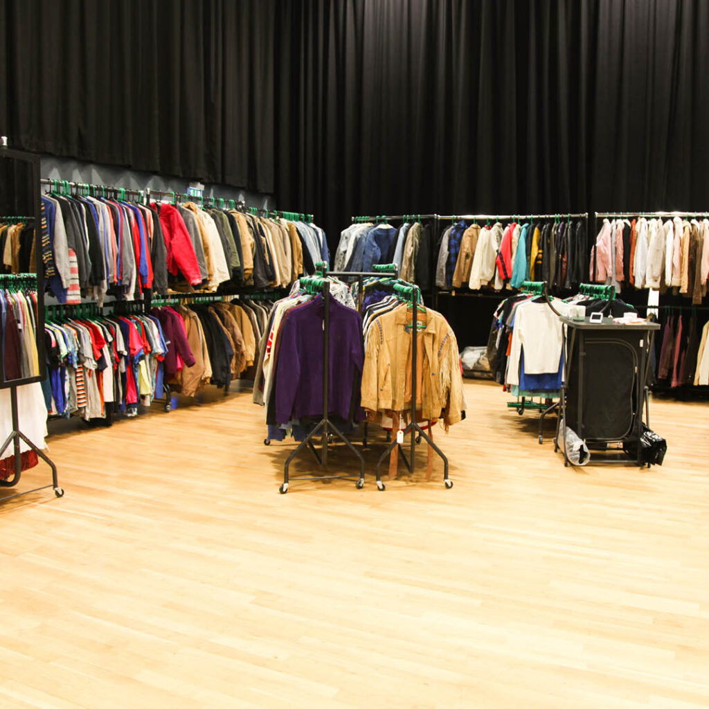 A wooden floored room is filled with racks of vintage clothes and retro streetwear.