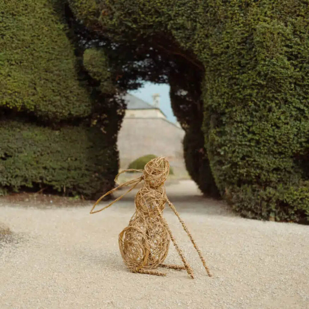A sculpture of a hare woven out of willow stands proudly in front of a green hedge in Raby Castle's gardens.