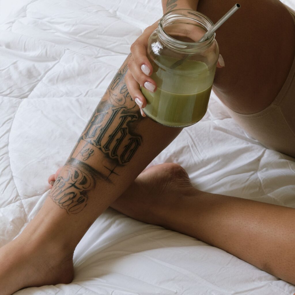 A woman is sitting on her bed drinking an iced match