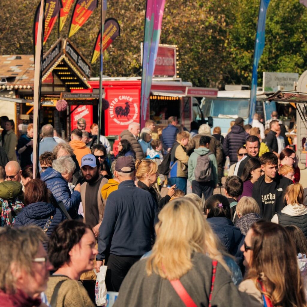 Crowds of people walk around at Chester-le-EATS food and drink festival. Food vans line the trees in the background.