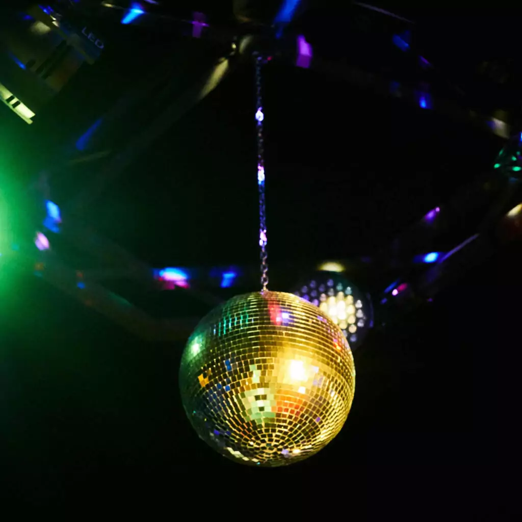 A large disco ball hangs from a black ceiling. Multi coloured shards of light glimmer around it.