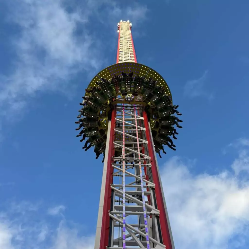 The Drop Tower ride stands against a bright blue sky. People's legs dangle from the seats encircling the middle tower. This is one of the rides at The Hopping funfair this summer.