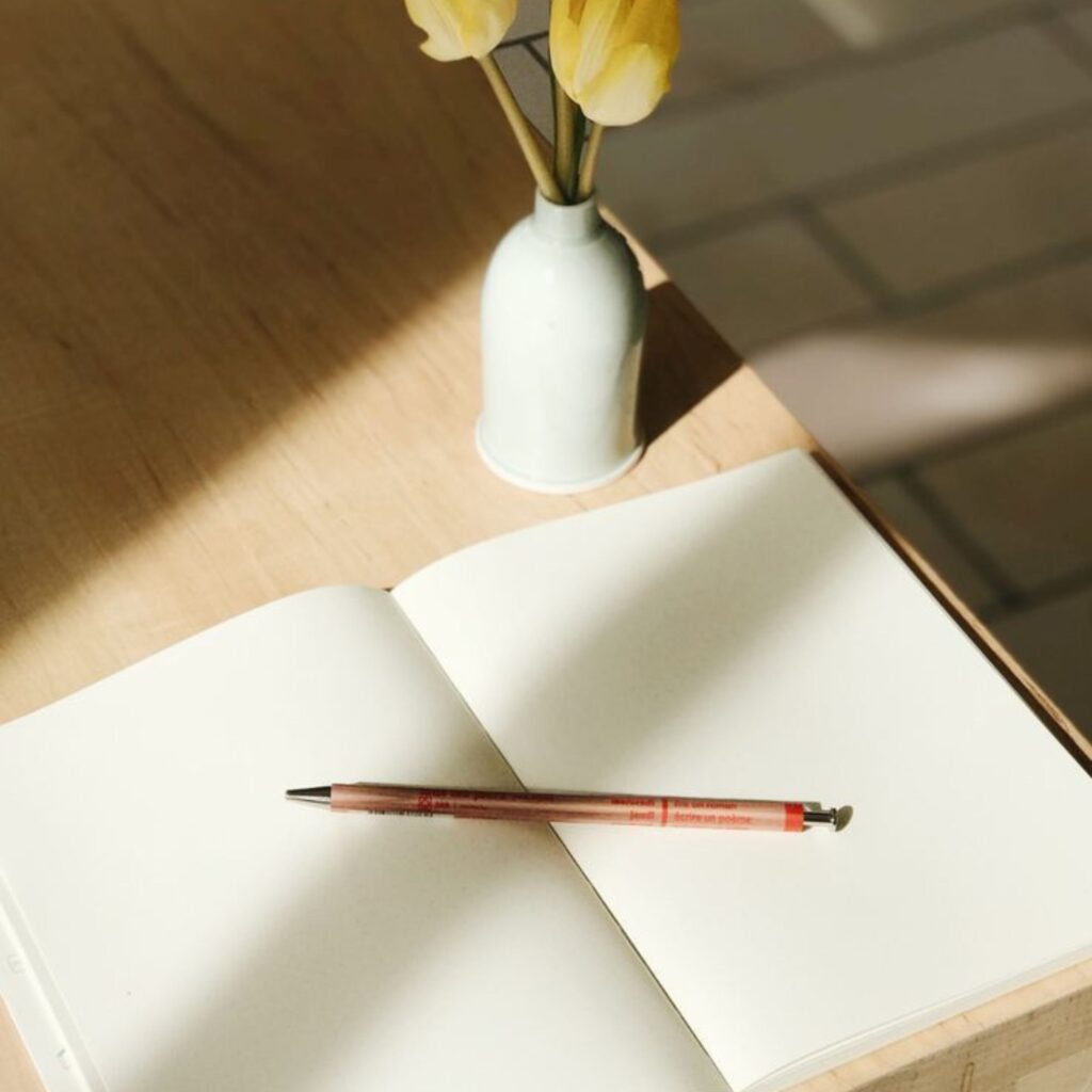 Open notebook on the table with a pen and vase of flowers