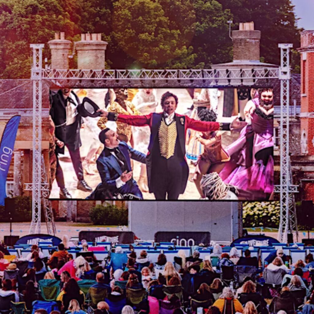 The Greatest Showman plays on a big open-air screen in the grounds of Alnwick Castle. People sit in front of it on camping chairs.