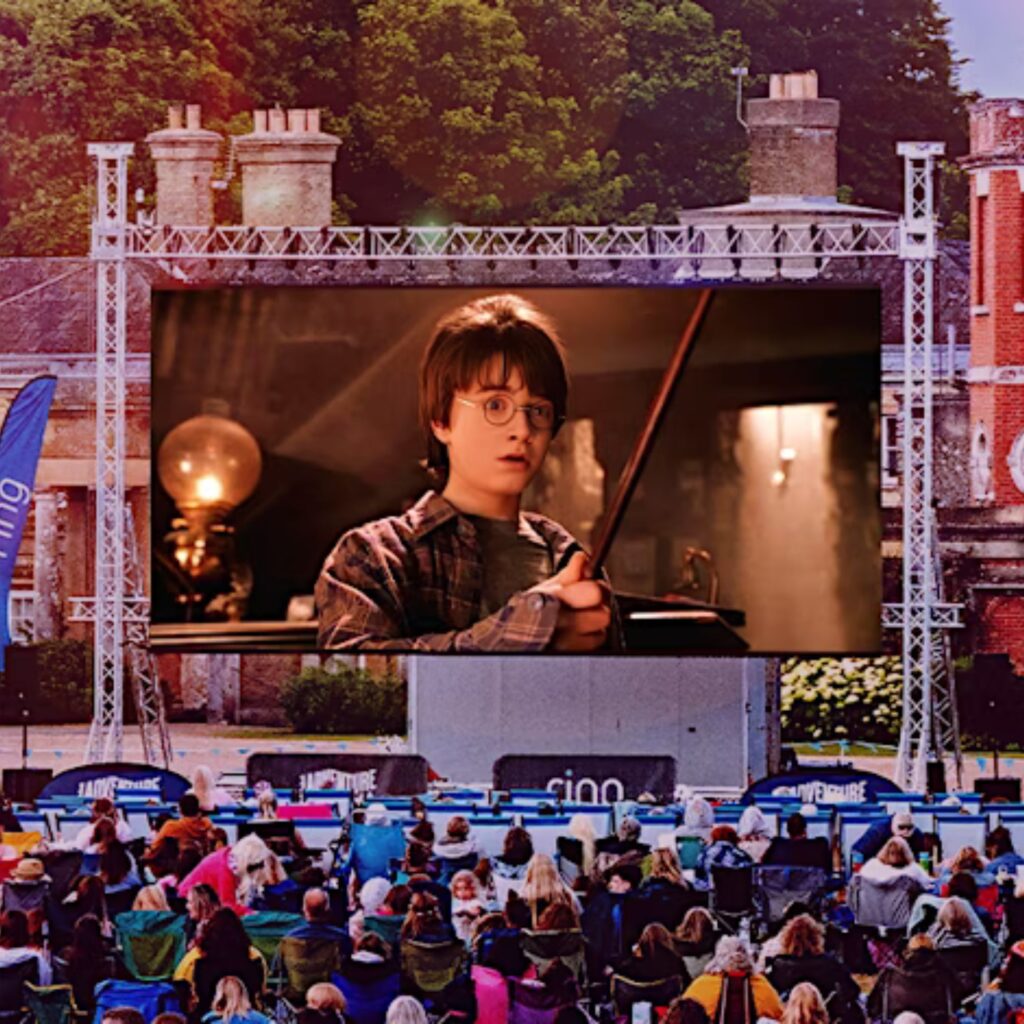Harry Potter and the Philosopher's Stone plays on a big open-air screen in the grounds of Alnwick Castle. People sit in front of it on camping chairs.