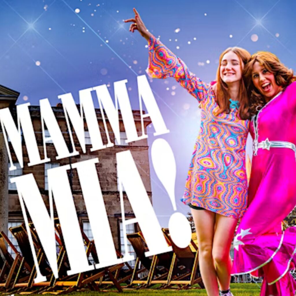 Two women dressed in pink disco style dresses raise their hands in the air as they sing along to an ABBA song. Big white words next to them say: Mamma Mia!