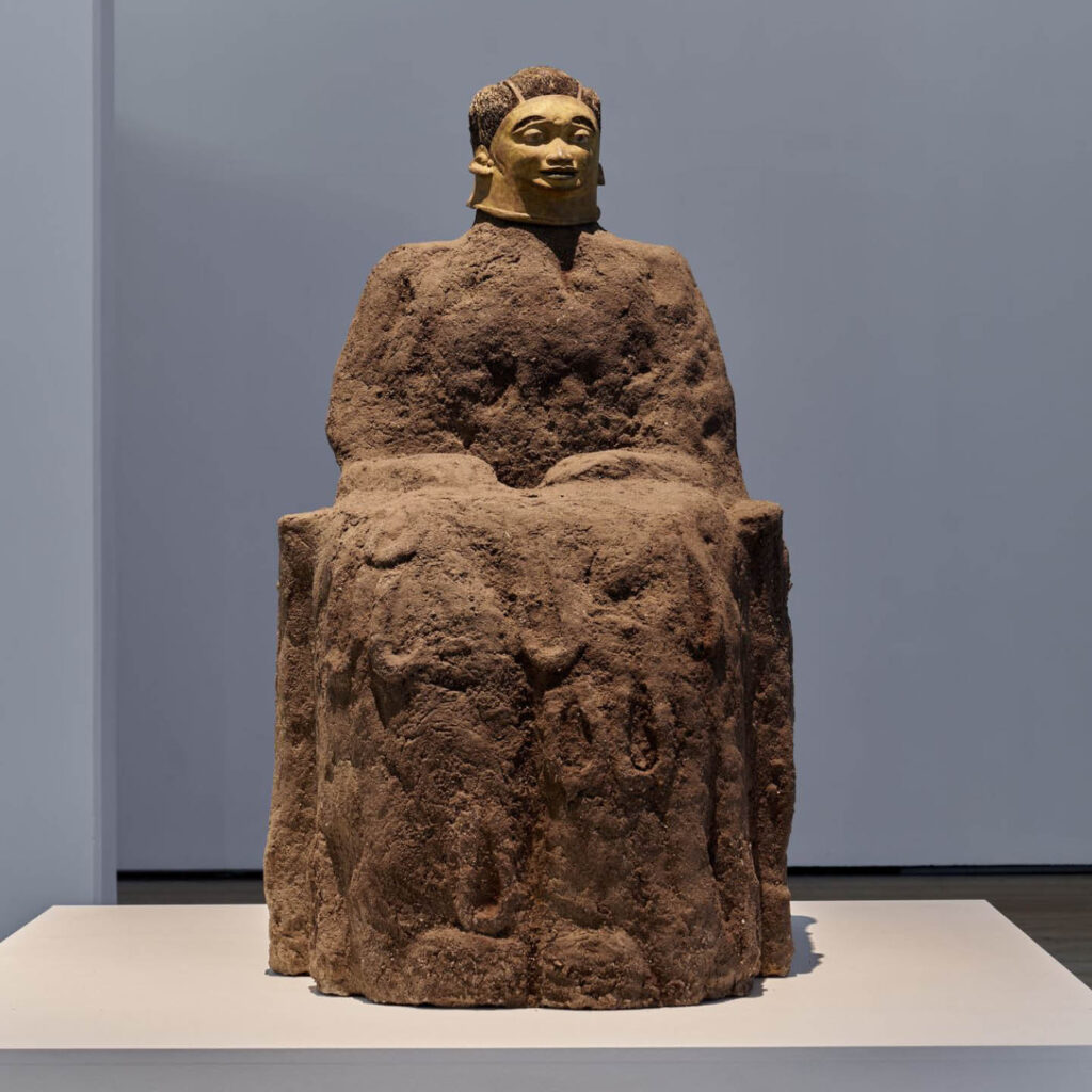 A large seated figure made from mud. A death mask has been placed on its face. This is part of Ali Cherri's How I Am Monument exhibition at BALTIC.