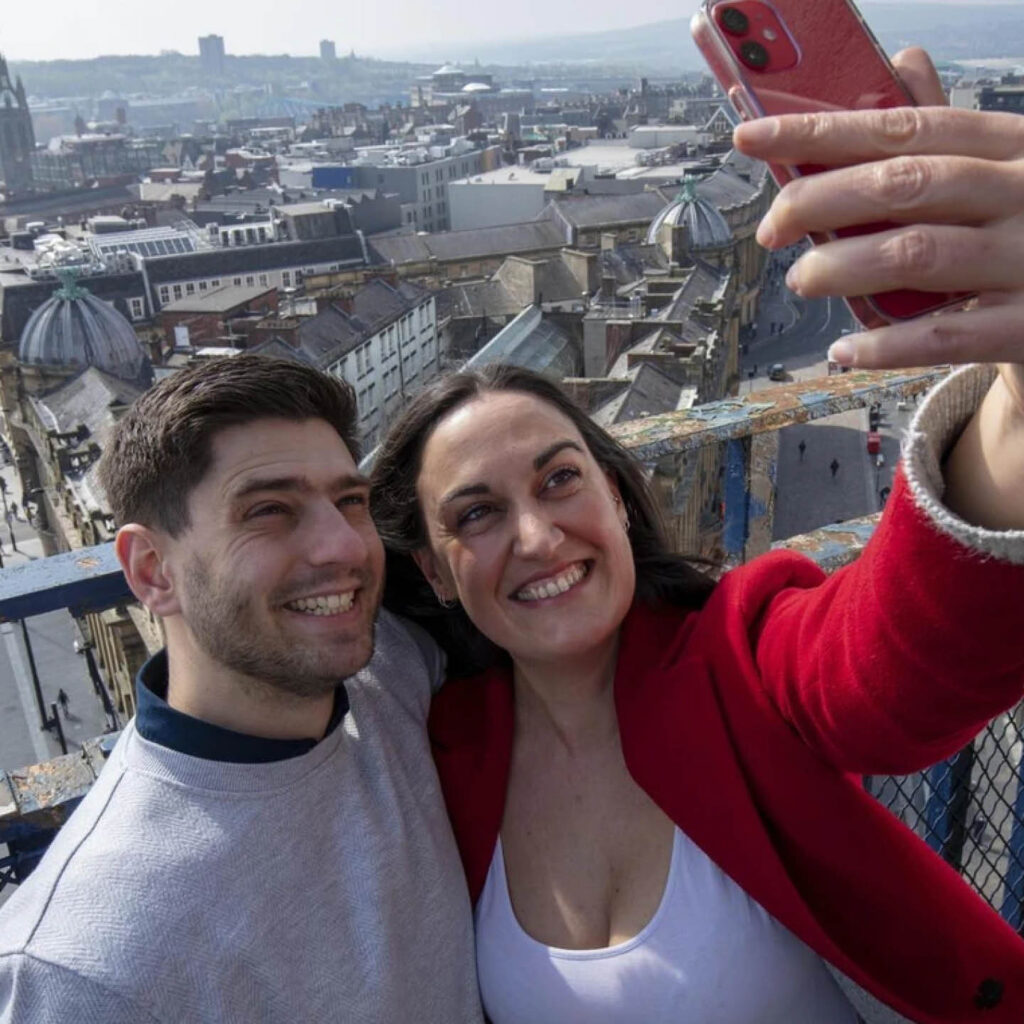 A couple grin as they take a selfie at the top of Greys Monument in Newcastle. Behind them, the city stretches into the distance.