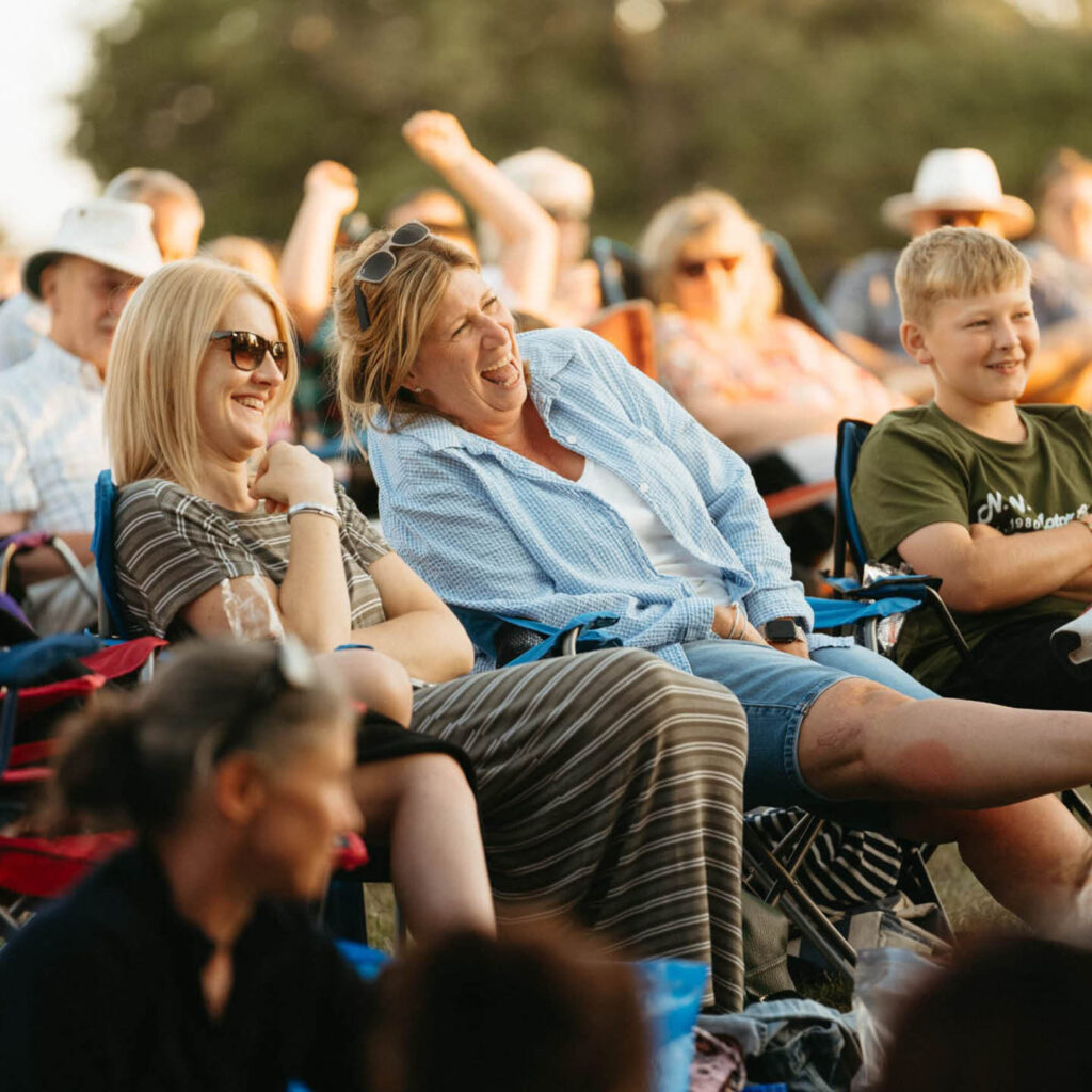 Two women and a boy laugh as they sit on deck chairs in Raby Castle's grounds. They are enjoying one of the open-air cinema sing-along shows.