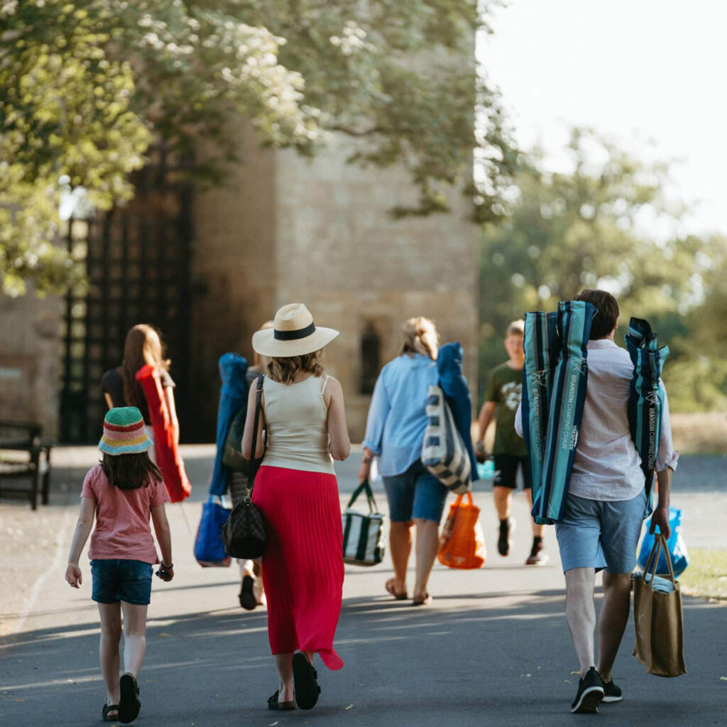A family carry folded chairs and picnic bags as they walk along a path at Raby Castle. They are heading for one of the Castle's open air cinema days.
