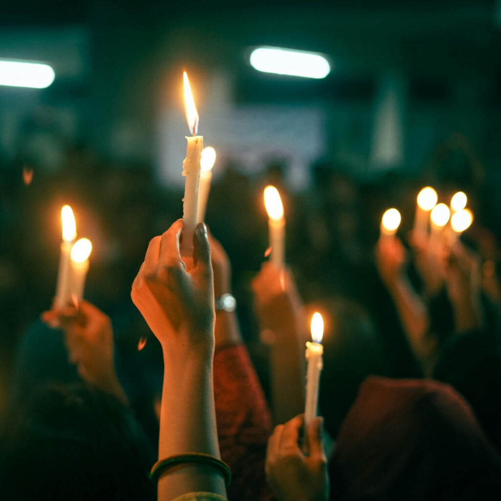 Hands hold up lit candles in the air.