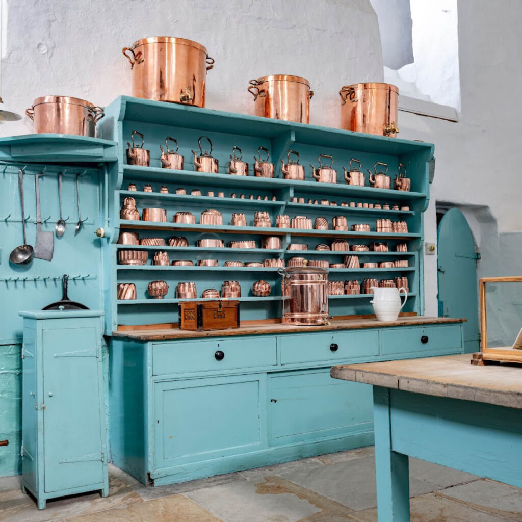 A variety of copper pans and pots line a big blue cabinet in the kitchen at Raby Castle.