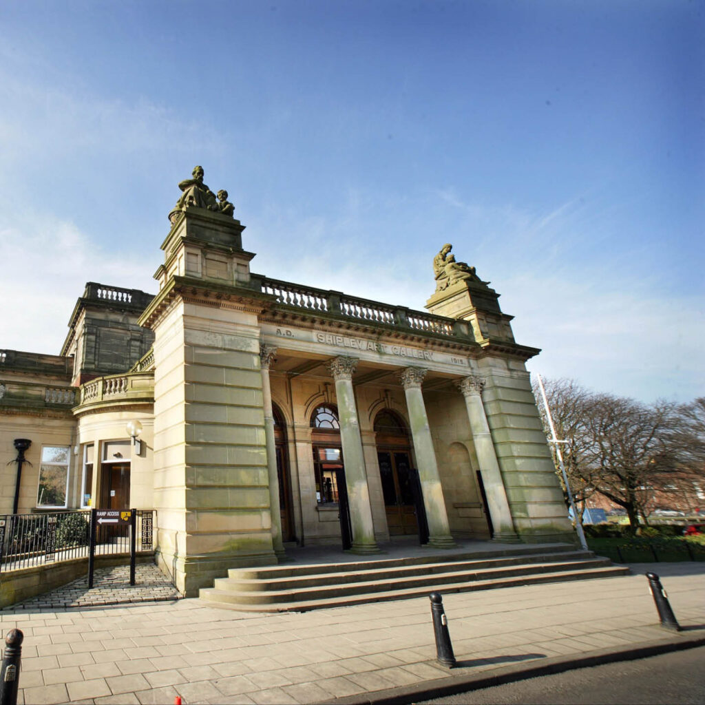 The stone building of Shipley Art Gallery beneath a clear blue sky.