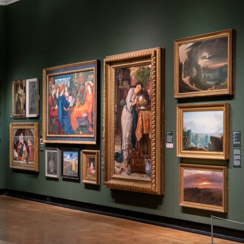 A dark green, dimly lit wall inside the Laing Art Gallery. It is hung with several large paintings displayed in thick gold frames.