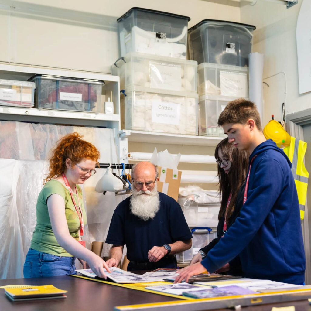 Three young people and an older man gather around a table in a back room of The Bowes Museum. They organise large archived prints spread on the table.