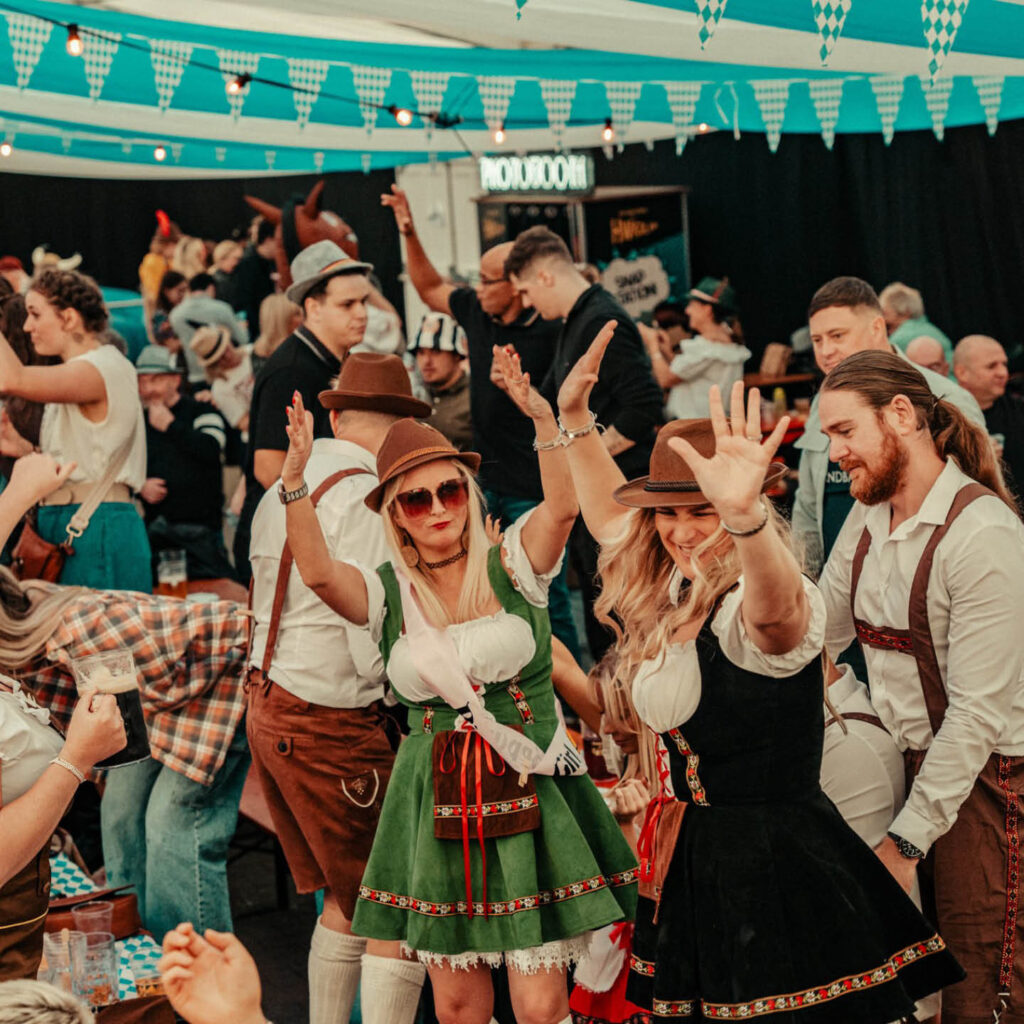 A crowd of men and women dressed in lederhosen and dirndls bust out their dance moves in a Bavarian beer tent during Oktoberfest, Newcastle.