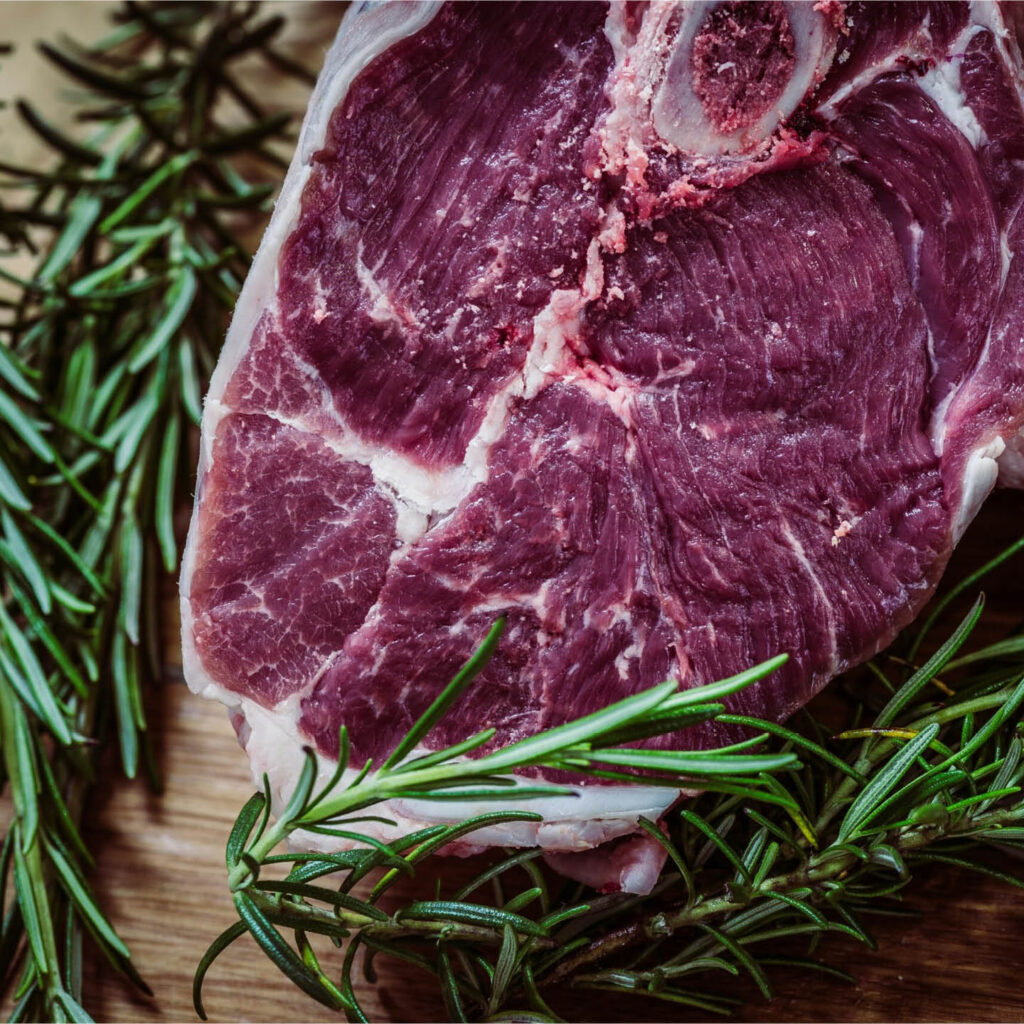 A raw steak of venison next to sprigs of rosemary.