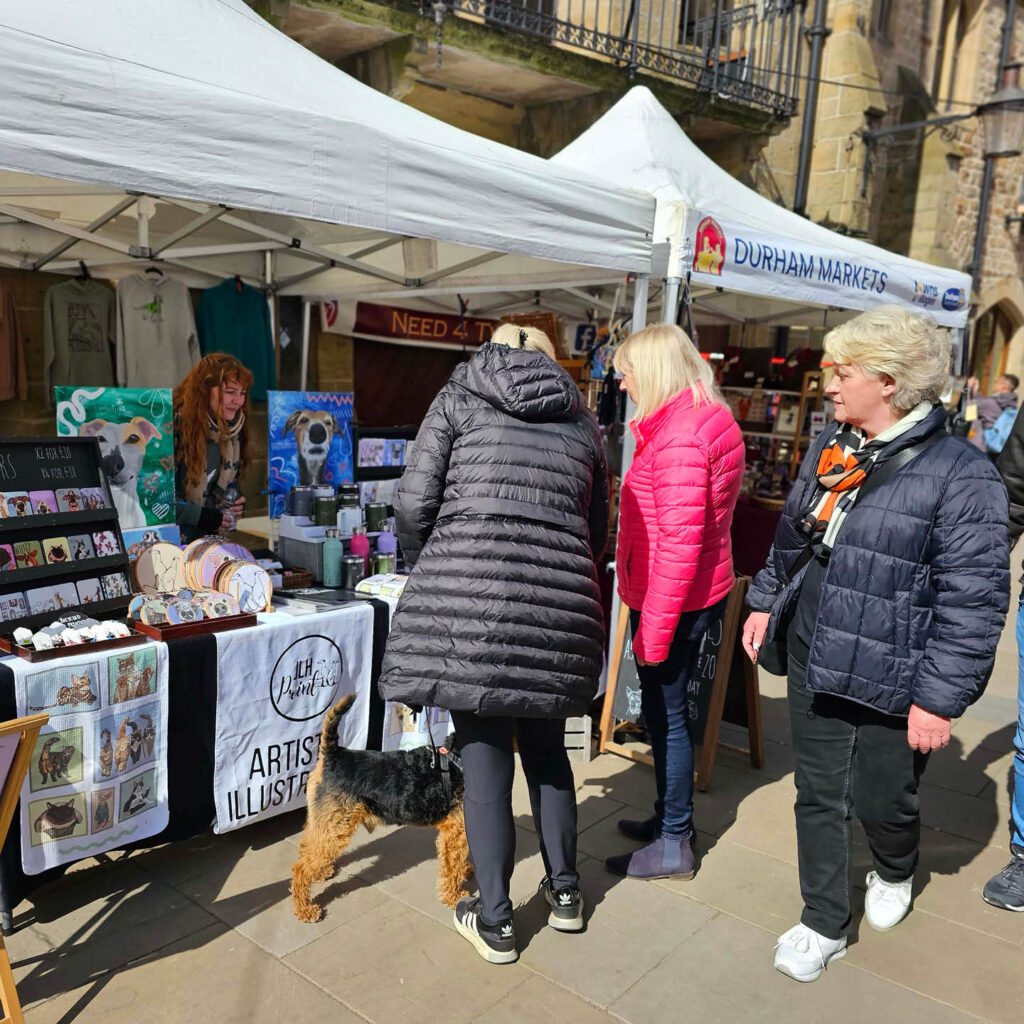 People gather around a stall selling pet art at Durham Market.