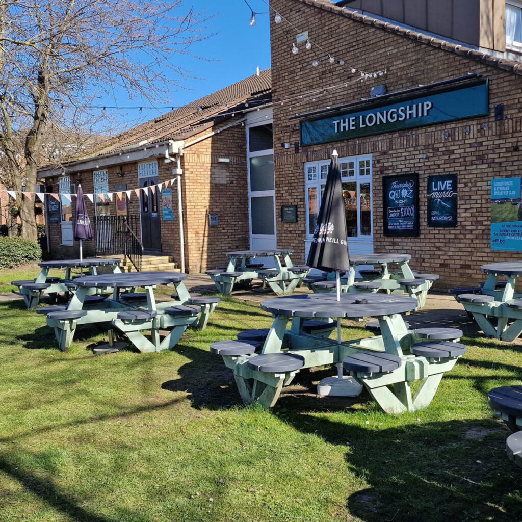 The sunny beer garden outside the Longship Pub in Hebburn. Bunting is strung between a tree and the building. The sky is bright blue.