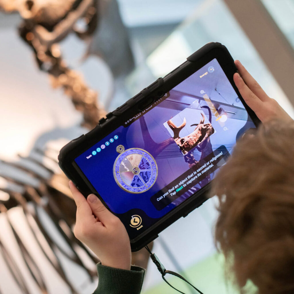 A child holds a tablet device in their hands. It shows a picture of an animal skeleton. It is part of the Time Odyssey experience at the Great North Museum: Hancock.