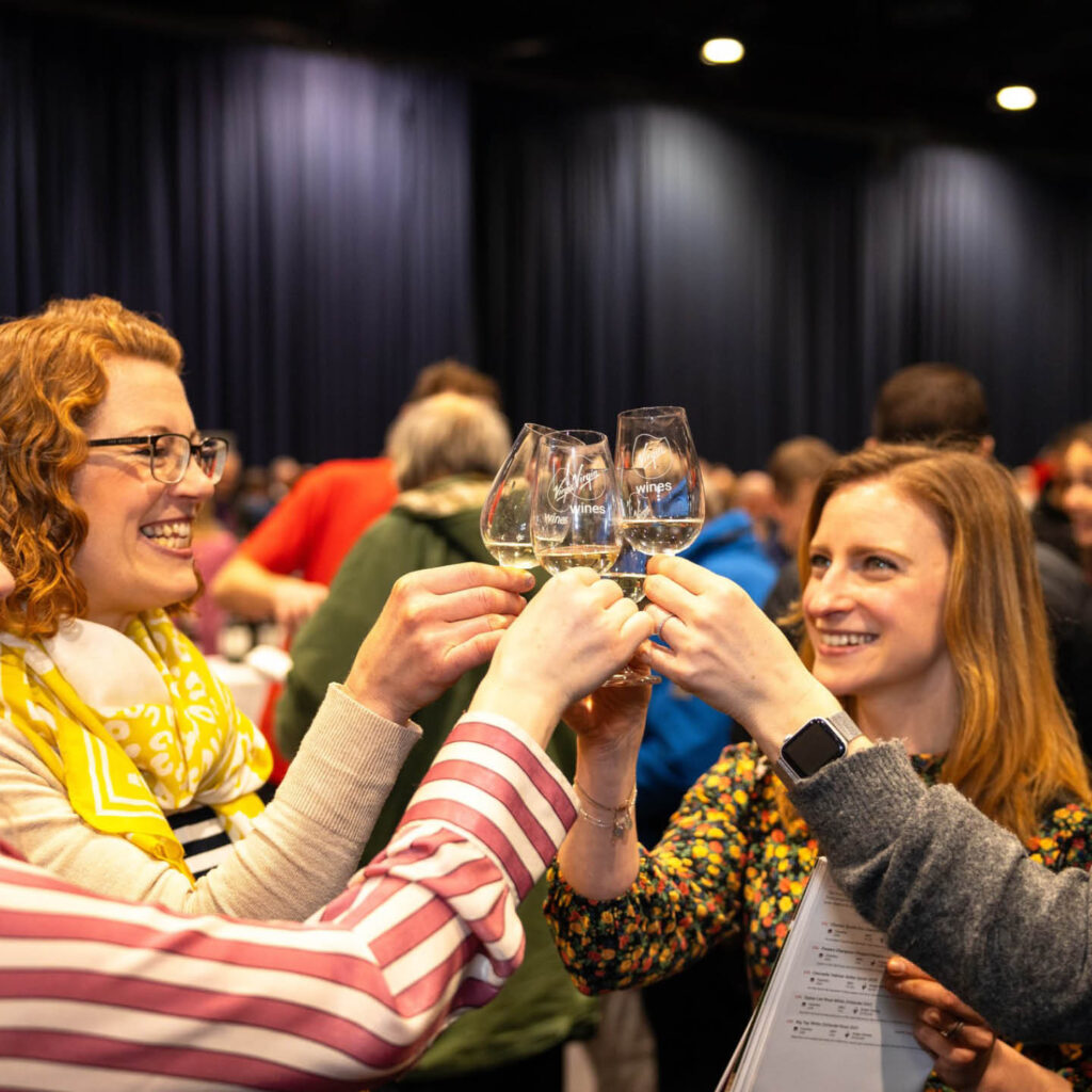 Four women smile as they clink wine glasses at a wine tasting event.