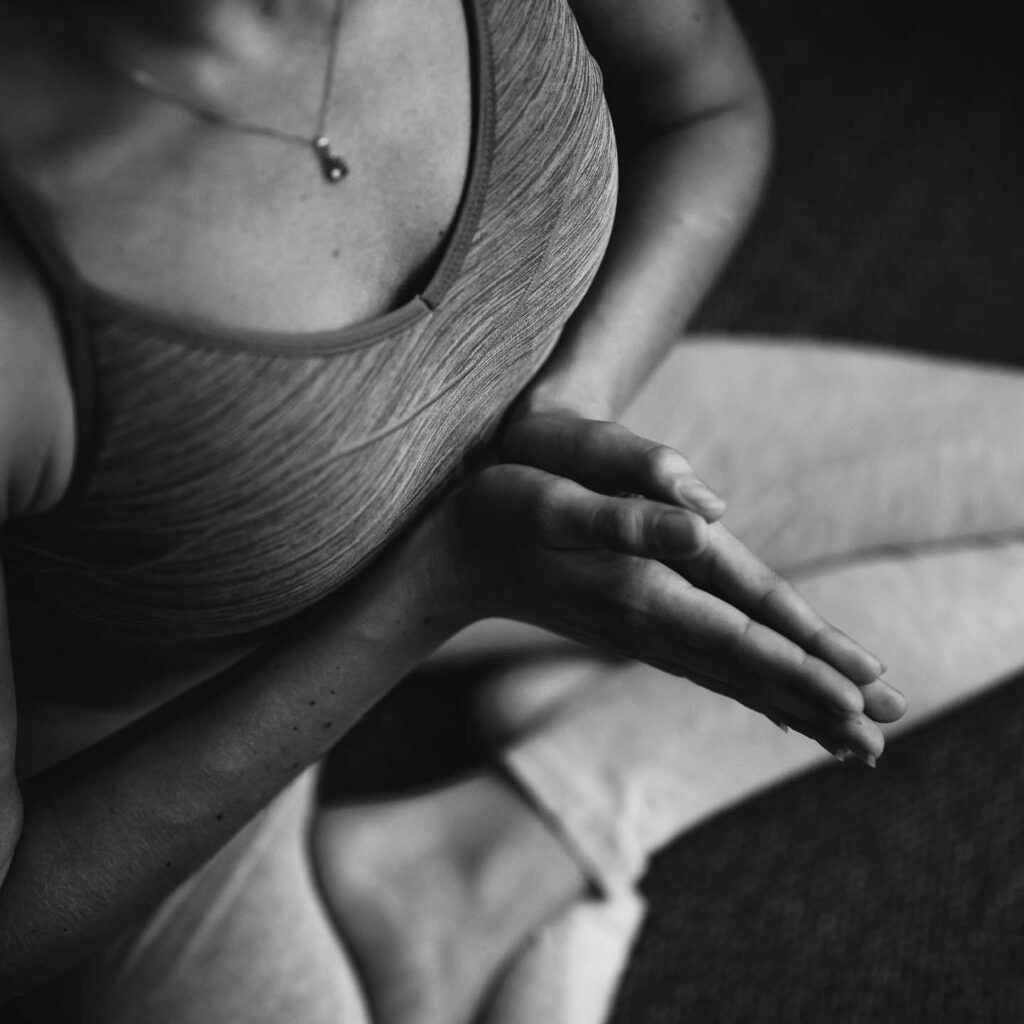 Black and white image of a woman. She sits cross legged with her palms pressed together in a yoga pose.