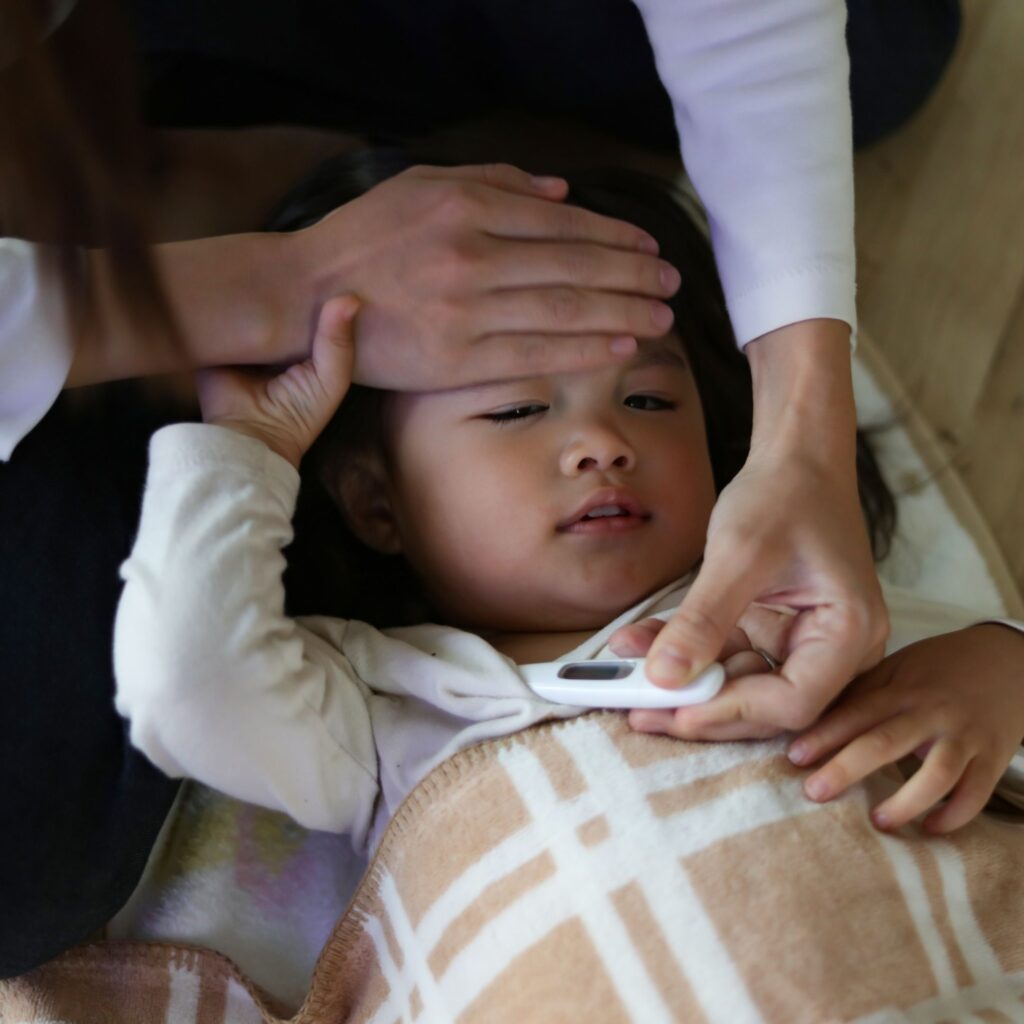 A child is sick with a fever as her mother checks her temperature