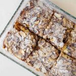 A bowl of baked almond oats topped with flaked almonds and a drizzle of honey, served warm with a spoon. The golden-brown oat bake has a soft, fluffy texture and is garnished with fresh berries for a wholesome breakfast.